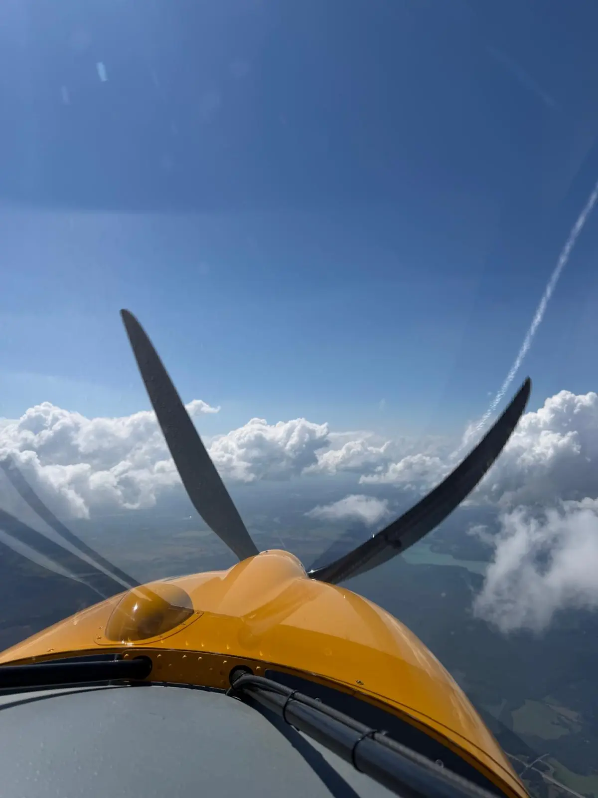 Blick aus dem Cockpit der gelben Maschine auf Propeller, Seen und Wolken
