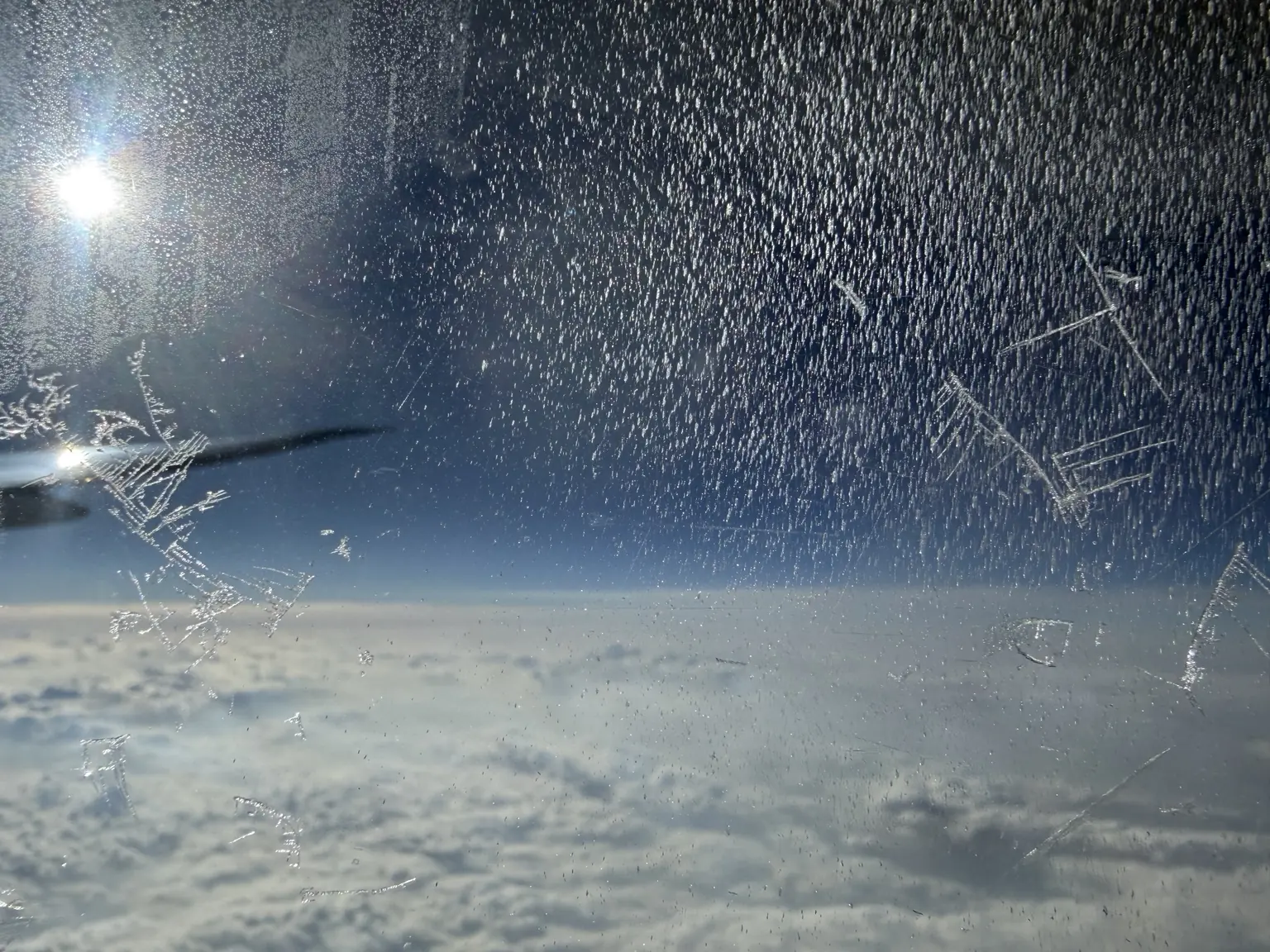 Sonne und Eiskristalle an der Scheibe über einer geschlossenen Wolkendecke