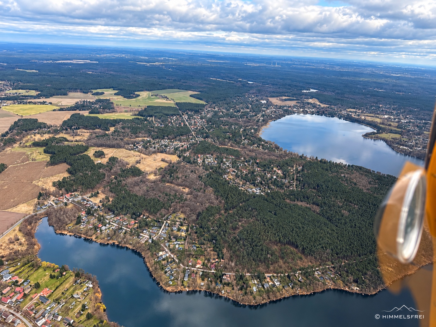 Eigenes Luftbild über Stolzenhagen bei Wandlitz: Seen, Wohnhäuser, Wälder und Felder unter einem weiten Wolkenhimmel, rechts ein Teil des Flugzeugs